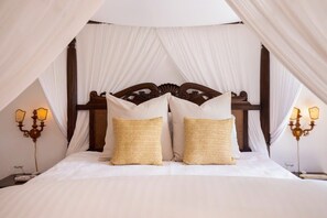 Een bed met hemelbed, twee bedlampen en een nachtkastje met lamp.