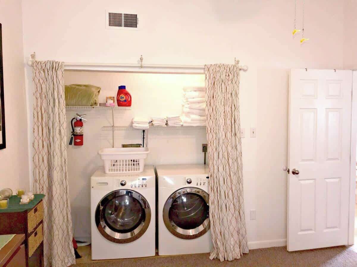 A laundry room with two front-loading washing machines, a drying rack, and a fire extinguisher.