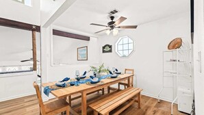 A dining area with a wooden table set for four, a ceiling fan, and a white shelving unit.