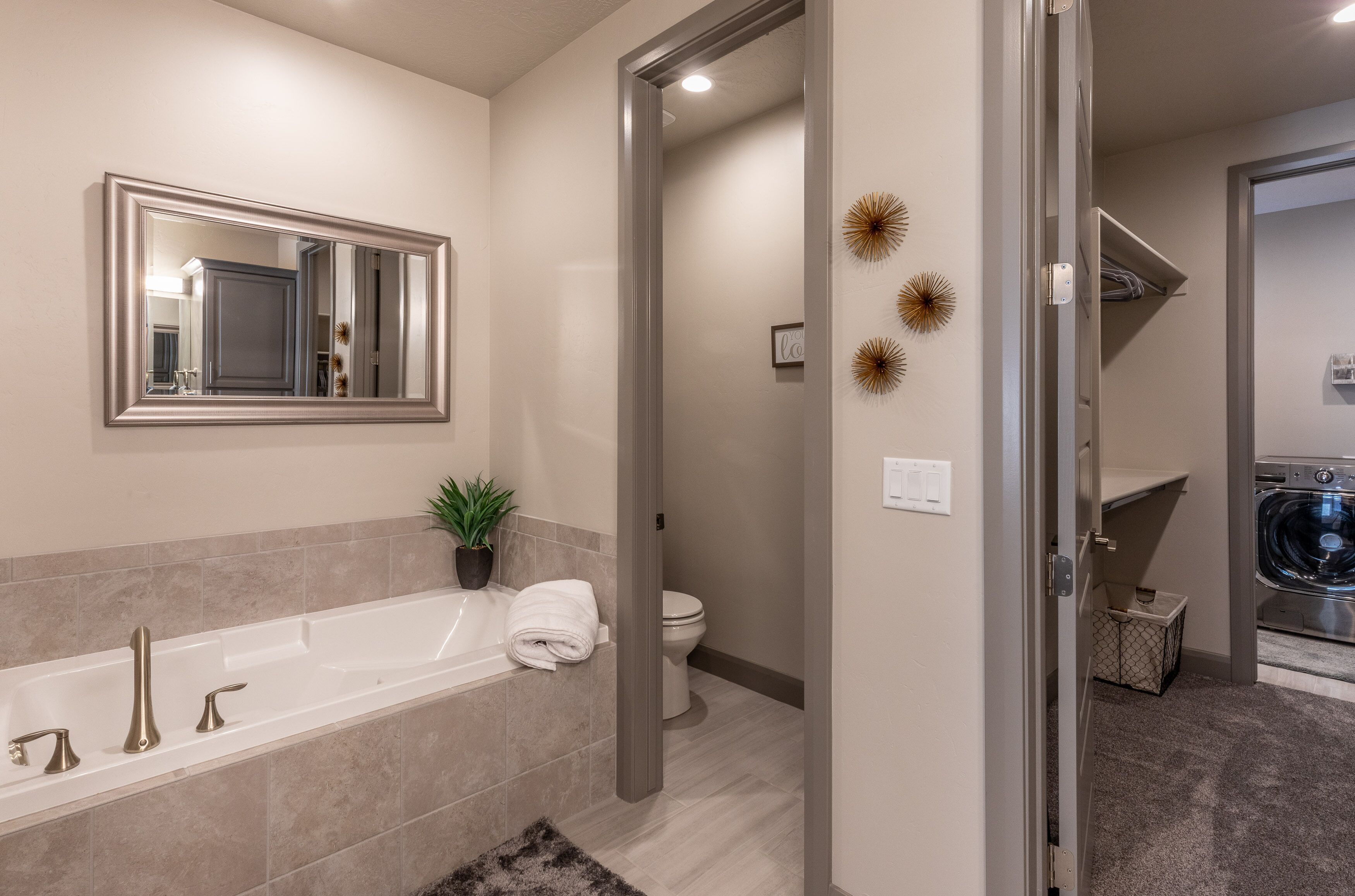 A modern bathroom with a bathtub, a toilet, and a shower area. There is a mirror above the bathtub and decorative wall art.