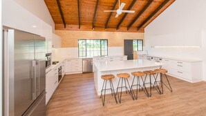 Una cocina moderna con armarios blancos, un refrigerador de acero inoxidable, taburetes de madera y un ventilador de techo.