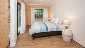 Un dormitorio con cama, mesita de noche, lámpara y ventana con cortinas.