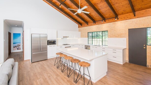 Una cocina moderna con armarios blancos, una isla grande con taburetes de bar, horno empotrado y refrigerador.