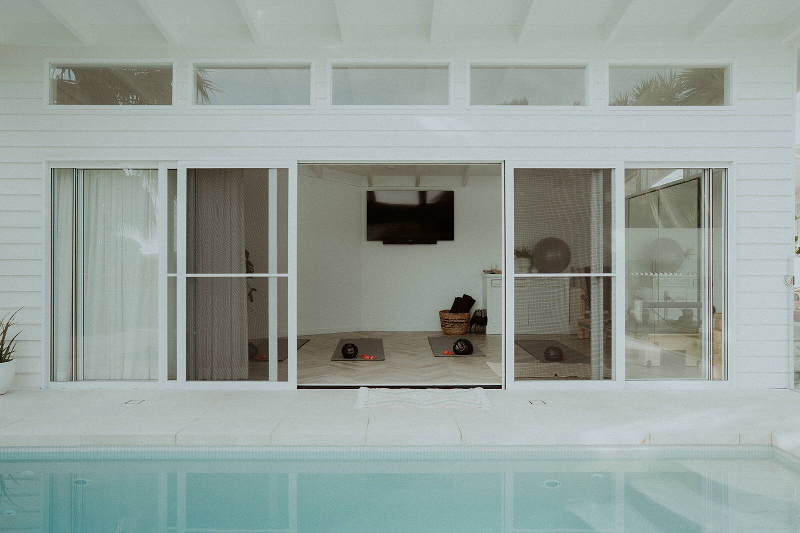 Une maison moderne dotée d’une piscine, de grandes portes-fenêtres coulissantes et d’un intérieur minimaliste.