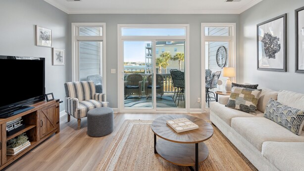 A living room with a television, striped armchair, grey ottoman, round coffee table, and a beige sofa. - Turtle Bay 21 - Riverview Condo - Pool (Folly Beach)