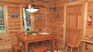 Interior de una cabaña de madera con una mesa de comedor, sillas, chimenea y un venado montado en la pared.