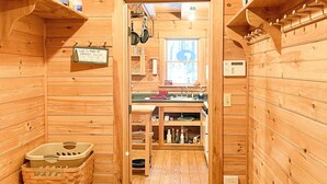 Interior de madera con un pasillo central que conduce a una zona de cocina, estantes con varios objetos y un letrero en la pared.