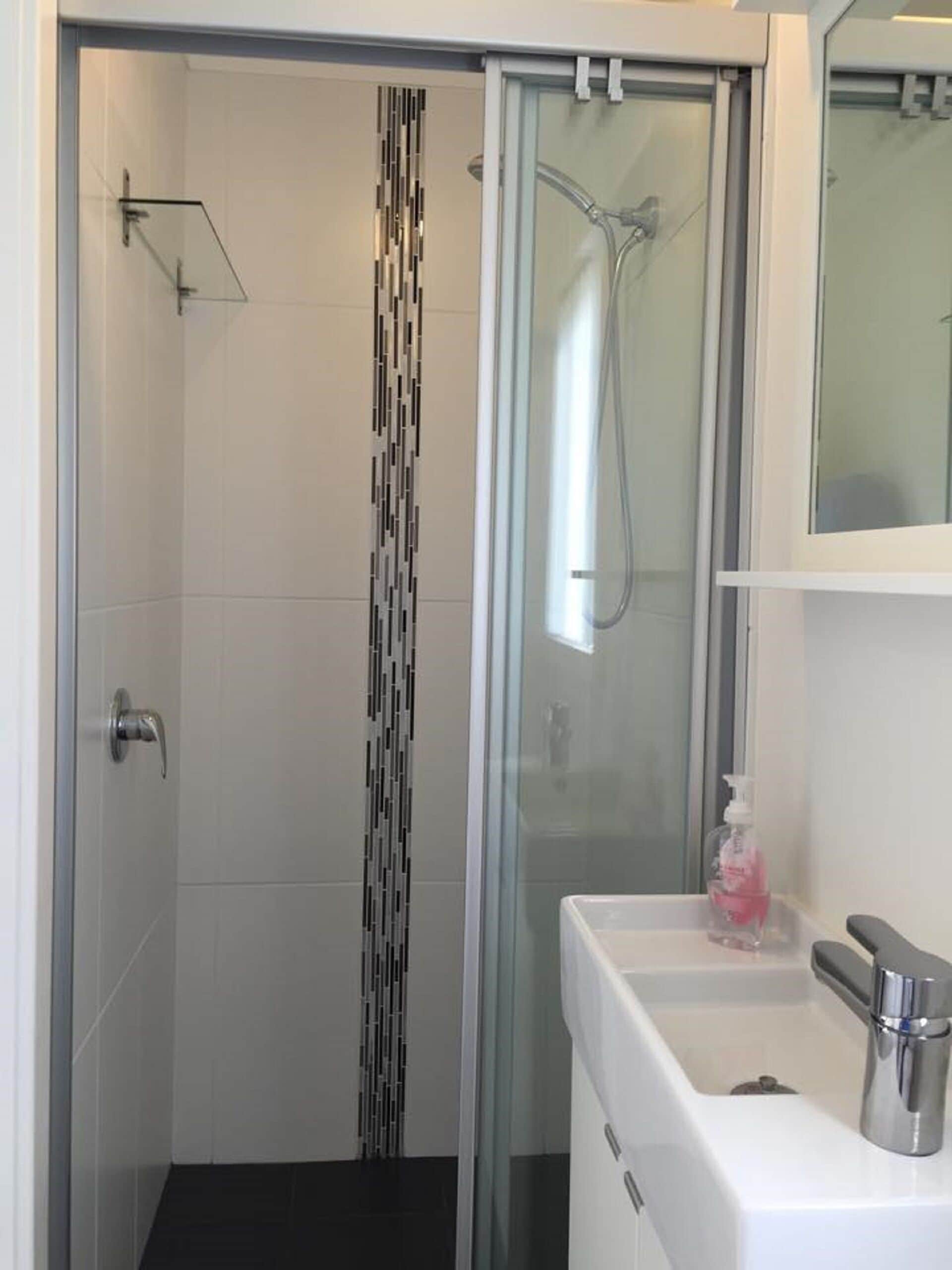 A modern bathroom with a glass shower enclosure, a white sink with a soap dispenser, and a mirror above the sink.