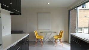 A modern kitchen with black cabinets, a white countertop, and a round glass table with two yellow chairs. - SeaEsta - Waterfront - Jervis Bay  - 5 minutes to Hyams Beach (Erowal Bay)