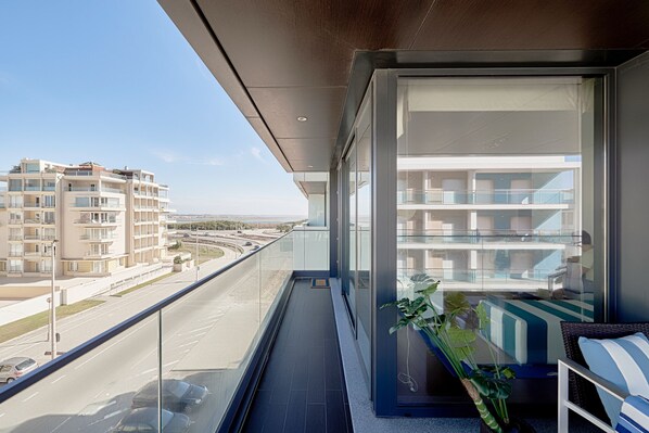 A balcony with a view of a road and buildings, a glass door, and a plant.