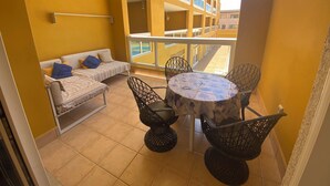 Een balkon met een bank, stoelen en een tafel, met uitzicht op een gebouw met gele muren.