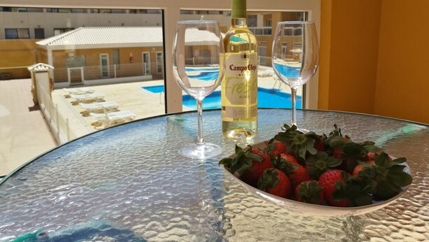 Een tafel met een fles Campo Viejo RIOJA FRESH BLENDED wijn, twee wijnglazen en een schaal verse aardbeien op een balkon met uitzicht op een zwembad.