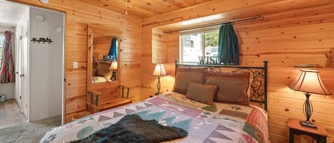 Un dormitorio acogedor con techo de madera, una cama con colcha estampada, una mesita de noche con lámpara y una ventana con vistas.