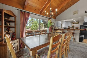 A dining area with a wooden table and chairs, a chandelier, and a view of the outdoors.