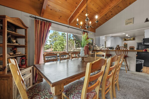 A dining area with a wooden table and chairs, a chandelier, and a view of the outdoors.