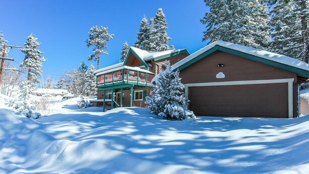 Een huis bedekt met sneeuw met een garage, omringd door bomen en een helderblauwe lucht.