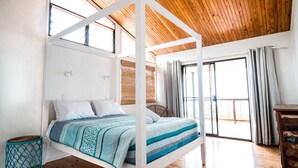 A high-ceilinged bedroom with a wooden ceiling, a bed with a striped blanket, a wicker chair, and a view of the outdoors through large windows. - Pets Allowed - This large family beach house also has great ocean and... (Point Lookout)