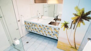 Ein Badezimmer mit Duschkabine aus Glas, Toilette, Waschbecken mit gemustertem Ablagetisch und Spiegel über dem Waschbecken.