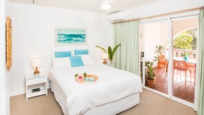 Ein geräumiges Schlafzimmer mit einem großen Bett, einem Gemälde des Ozeans, einem Balkon mit Gartenmöbeln und einer Glastür.