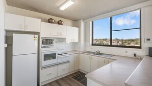 Cocina moderna con armarios blancos, estufa, microondas y un amplio ventanal con vista a la ciudad.