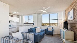 Una sala de estar moderna con un sofá, sillones, un televisor y una cocina al fondo.