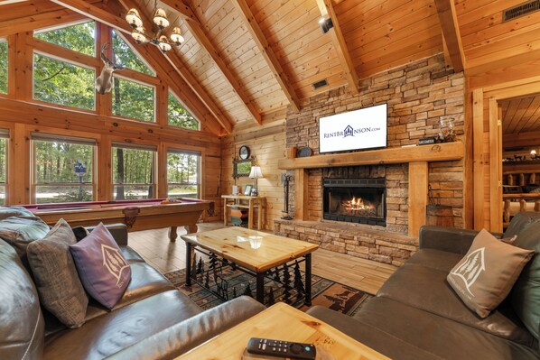 L’intérieur chaleureux d’un chalet avec une cheminée, des murs en bois et une grande fenêtre donnant sur une forêt.