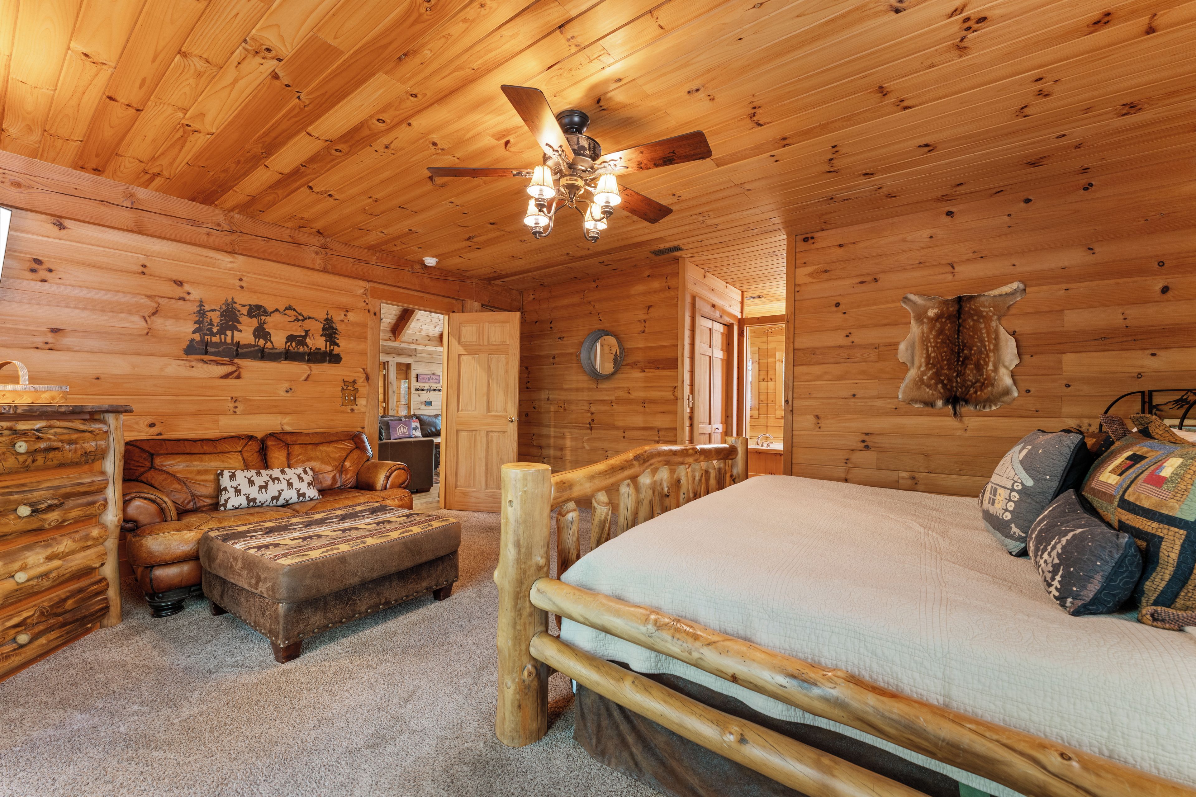 A log cabin interior with a bed, a sofa, a wooden headboard, a ceiling fan, and a wall-mounted mirror.