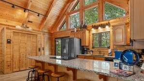 A wooden cabin kitchen with a granite countertop, wooden stools, and a large refrigerator. - Luxury Log Cabin Near Thunder Ridge_Pvt Fenced Yard & HotTub_Billiards_EV Car Charger_Free Tickets (Ridgedale)