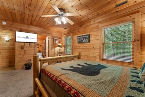L’intérieur d’un chalet en bois, avec un lit, un ventilateur de plafond et une pancarte sur laquelle on peut lire : « Bienvenue au chalet ».