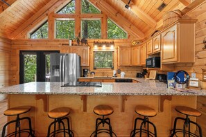 A spacious kitchen with a large island, bar stools, and a view of the outdoors through the windows.