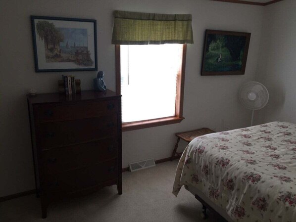 A bedroom with a bed, dresser, window, and two framed pictures on the wall.