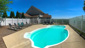 Ein Swimmingpool mit weißem Rand, umgeben von einem weißen Zaun, und ein Haus im Hintergrund.