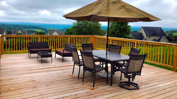 Eine Holzterrasse mit Tisch und Stühlen, einem großen Sonnenschirm und Blick auf eine grüne Landschaft.