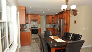 Eine moderne Küche mit Holzschränken, einem Edelstahlkühlschrank und einem Essbereich mit schwarzem Tisch und Stühlen.