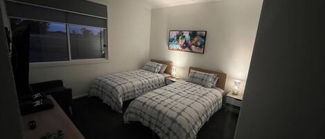 A bedroom with two beds, a ceiling fan, a window, and a painting on the wall.