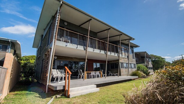 Een modern huis met twee verdiepingen, een balkon, een overdekt terras en een verzorgd gazon.