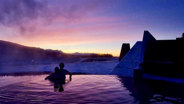 En person i en jacuzzi med et bjergrigt landskab i baggrunden.