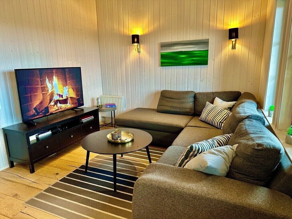 A modern living room with a sectional sofa, a television, a coffee table, and two wall-mounted lamps.