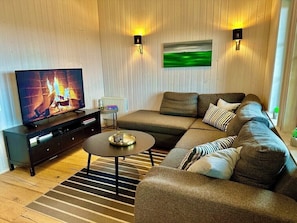 Una sala de estar moderna con un sofá modular, una televisión, una mesa de centro y dos lámparas fijadas a la pared.
