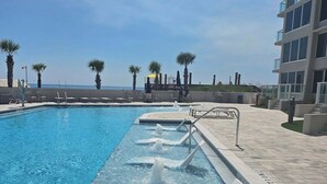 A swimming pool with a water slide, surrounded by palm trees and a building with balconies. - BEACHSIDE 2 SANDESTIN SUMMER DISCOUNTS! BEACH FRONT 1 BR NEW POOL & HOT TUB! (Miramar Beach)