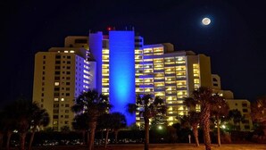 A multi-story hotel with illuminated balconies and a prominent blue-lit central tower. - BEACHSIDE 2 SANDESTIN SUMMER DISCOUNTS! BEACH FRONT 1 BR NEW POOL & HOT TUB! (Miramar Beach)