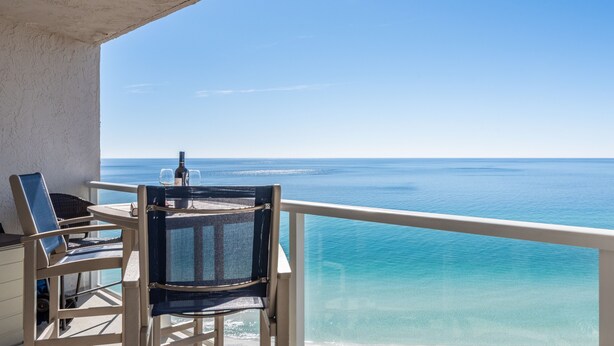 A balcony with a table and chairs overlooking a clear blue sea. - BEACHSIDE 2 SANDESTIN SUMMER DISCOUNTS! BEACH FRONT 1 BR NEW POOL & HOT TUB! (Miramar Beach)