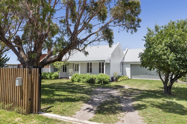 A residential house with a front yard, a wooden fence, and a large tree.