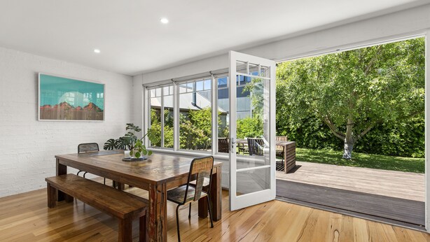 A spacious dining area with a wooden table and benches, large windows offering a view of a garden and a modern building. - Pet friendly Riverside Retreat (Barwon Heads)