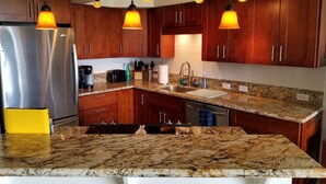 A modern kitchen with wooden cabinets, granite countertops, a stainless steel refrigerator, and pendant lighting.