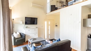 A compact living space with a sofa, a small table, a television, and a kitchenette area. - ALLAMBIE COTTAGES - VILLA 2: Bright (Bright)