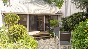 A small house with a porch, a chair, and a table. - ALLAMBIE COTTAGES - VILLA 2: Bright (Bright)