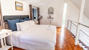 A bedroom with a large bed, a bedside table, a mirror, and a view of a wooden staircase. - ALLAMBIE COTTAGES - VILLA 2: Bright (Bright)