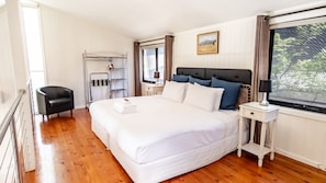 A hotel room with a large bed, a bedside table, a chair, a window with curtains, and a painting on the wall.