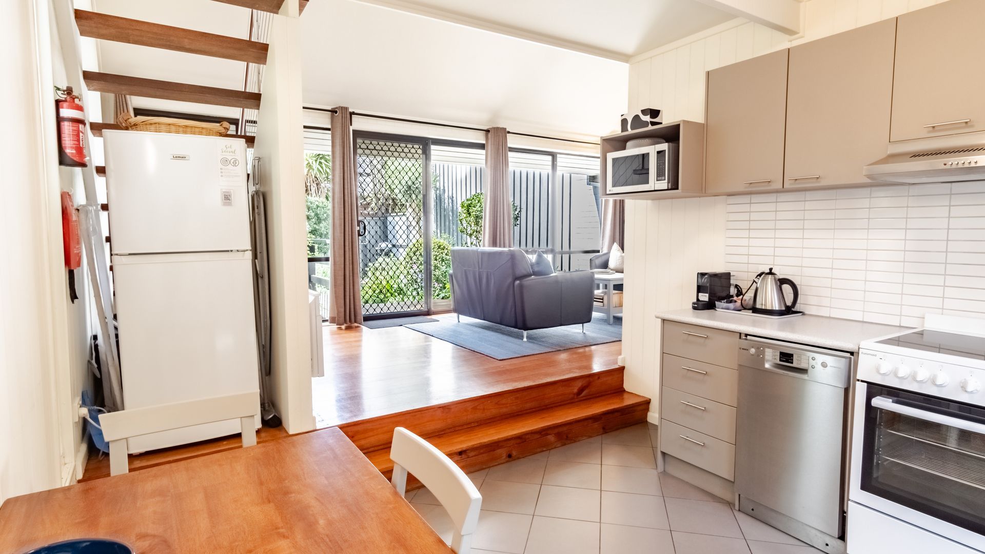 A compact kitchen with a refrigerator, microwave, stove, and dishwasher. There is a seating area with a sofa and a dining table.